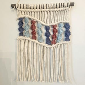 May include: A macrame wall hanging with a white cotton cord and blue, red, and white yarn woven into a wave pattern.
