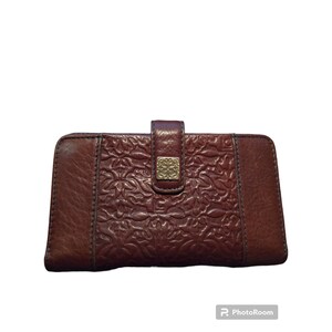 May include: A brown leather wallet with an embossed floral design. The wallet has a gold-toned clasp and a flap closure.