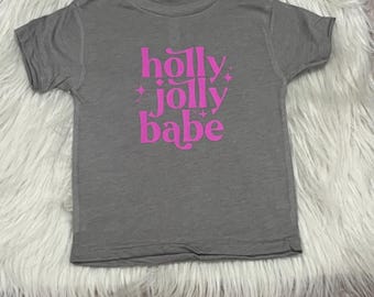 May include: Gray short-sleeved t-shirt with a pink graphic that says "holly jolly babe".