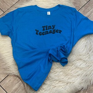May include: A bright blue t-shirt with the text "Tiny Teenager" printed in black.