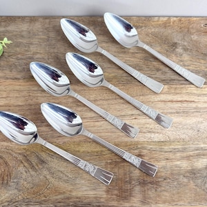 Peut inclure: Six cuillères argentées avec une surface réfléchissante sont disposées sur une surface en bois. Les cuillères ont un motif décoratif sur le manche. Les cuillères sont inclinées sur le cadre.