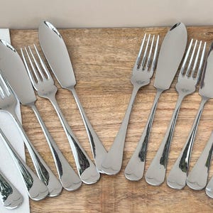 Peut inclure: Ensemble de fourchettes et de couteaux à beurre en acier inoxydable disposés sur une surface en bois. Les couverts ont une finition brillante et réfléchissante. Les fourchettes ont quatre dents et les couteaux une lame arrondie.