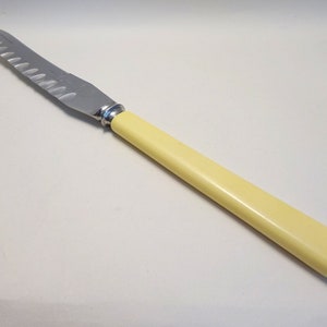 May include: A stainless steel butter knife with a serrated edge and a yellow plastic handle.