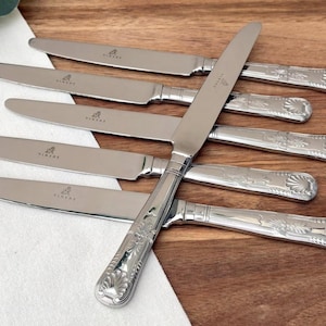 May include: Six stainless steel knives with decorative handles, arranged on a wooden surface. The knives have a shiny finish and a floral pattern on the handles. The blades are smooth and sharp, ideal for dining.