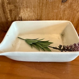 May include: A white ceramic baking dish with a pouring spout. The dish is empty and has a light green sprig of greenery inside.