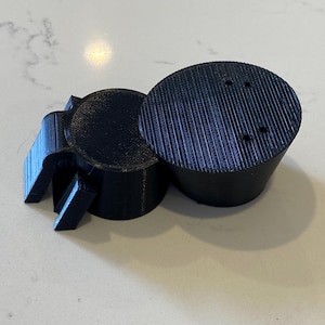 May include: A black 3D-printed object resembling a spider. The object has a circular body with three small holes and a textured surface. It also has multiple leg-like appendages extending from the body.