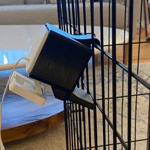 May include: A black metal cage with a white and black device attached to the side. The device has a white cord attached to it.