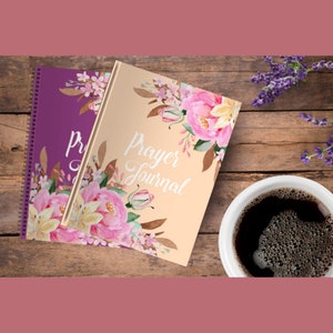 Puede incluir: Dos diarios de oraci&oacute;n en espiral con dise&ntilde;os florales. El diario superior es melocot&oacute;n con el texto "Prayer Journal" y el diario inferior es morado con el texto "Prayer Journal".