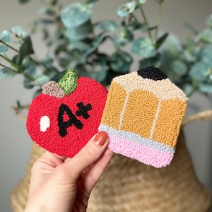 May include: Two felt crafts, an apple with an A+ on it and a pencil, both in bright colors.