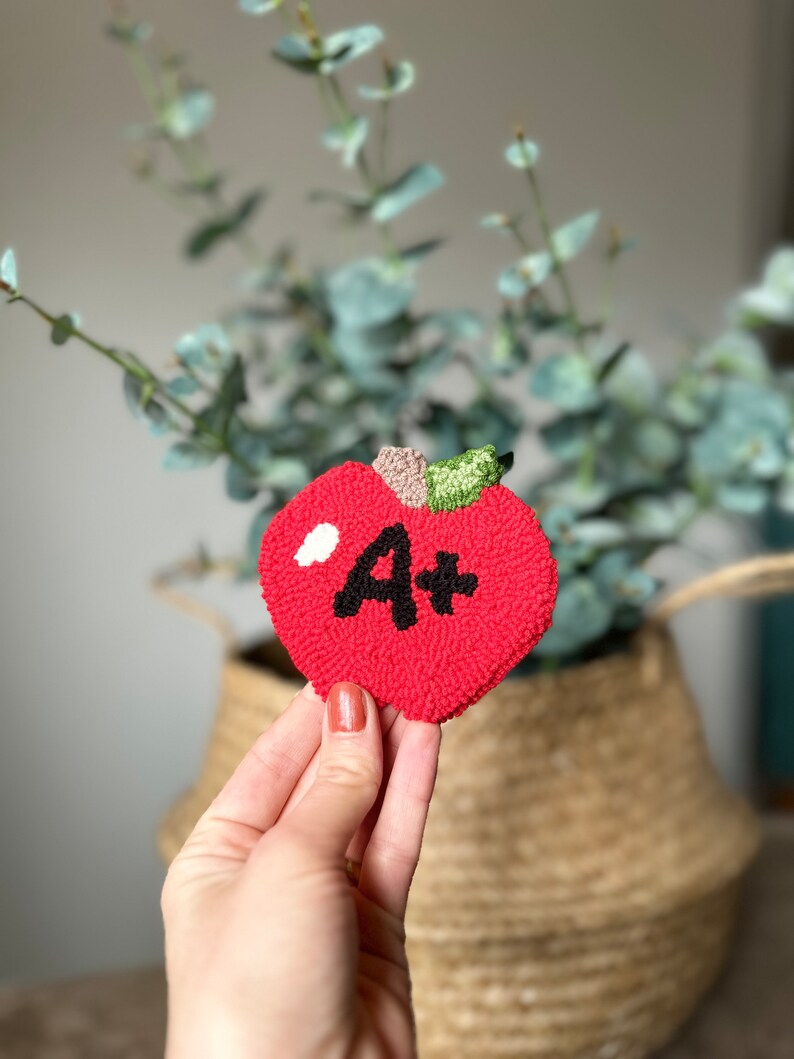 May include: A red felt apple with a white and black felt "A+" on it.