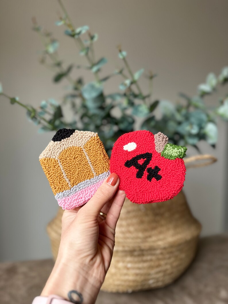 May include: A red felt apple with a white stem and a black "A+" on it. A yellow and brown felt pencil with a pink eraser is next to the apple.