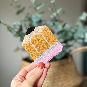 May include: A yellow, pink, and gray pencil shaped rug made with yarn. The rug is made with a technique called punch needle.