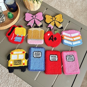 May include: A collection of colorful, textured school-themed items, including a pink bow, yellow bow, red backpack, pencil, red apple with "A+", stack of books, yellow school bus, and three notebooks in blue, red, and pink.