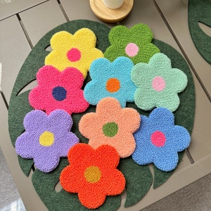 Op de afbeelding: Een set van acht kleurrijke, bloemvormige onderzetters met verschillende gekleurde centra. De onderzetters zijn gemaakt van een zacht, pluche materiaal en zijn perfect om een vleugje whimsy toe te voegen aan elk huis.