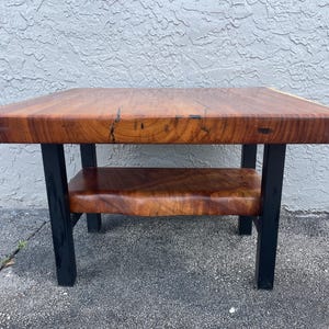 May include: A wooden coffee table with a natural wood finish and black metal legs. The table has a lower shelf.