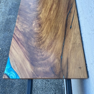 May include: A wooden table top with a blue resin inlay. The table top is made of natural wood with a rich brown color. The resin inlay is a swirling pattern of blue and green.