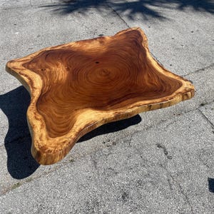 May include: A large, natural wood coffee table with a live edge and a rich brown color. The wood grain is visible and the table has a unique, organic shape.