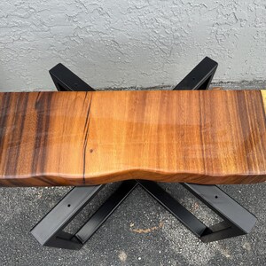 May include: A wooden bench with a live edge top and black metal legs. The wood has a natural grain pattern and a light brown color.