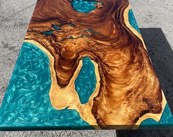 May include: A large wooden table top with a natural wood grain pattern and a turquoise blue epoxy resin fill. The resin has a swirling pattern and creates a unique design.