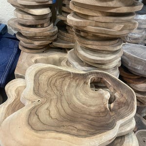May include: Stacks of unfinished wooden serving boards with organic shapes and natural wood grain patterns. Some boards have a handle-like cutout. The boards vary in size and are light brown in color.