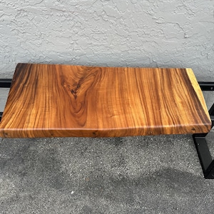 May include: A wooden bench with a live edge top and black metal legs. The wood is a rich brown color with a natural grain pattern.