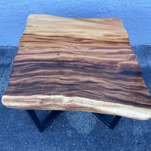 May include: A wooden coffee table with a live edge top and a black metal base. The table top has a natural wood grain pattern and a light brown color.