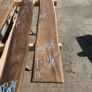 May include: Three unfinished wood slabs with live edges. The slabs are various lengths and widths, with measurements in inches written in blue marker. The wood has a natural grain and a warm brown color.