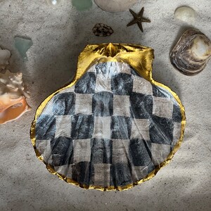 May include: A decorative seashell with a black and white checkered pattern and gold trim. The shell is made of a natural material and has a rustic, vintage look.