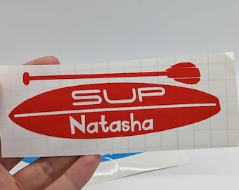 Op de afbeelding: Rode en witte vinyl sticker met een peddel en surfplank ontwerp. De tekst "SUP Natasha" staat op de sticker.