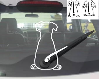 Op de afbeelding: Een witte vinyl sticker van een hondensilhouet op de achterruit van een auto. Het ontwerp toont een hond van achteren gezien, waarbij de staart is uitgelijnd met de achterruitenwisser, die als staart fungeert wanneer deze in beweging is.