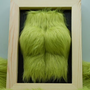 May include: A framed green fuzzy artwork with a wood frame. The fuzzy artwork is in the shape of a torso.