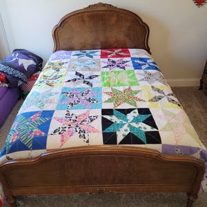 May include: A wooden bed frame with a headboard and footboard. The bed is covered with a colorful patchwork quilt with a star pattern.