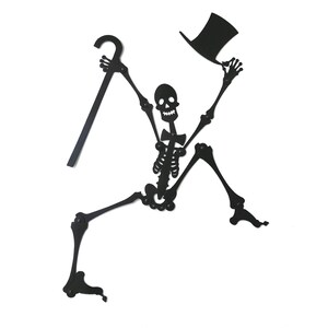 May include: A black metal skeleton silhouette with a top hat and cane. The skeleton is in a dancing pose with one leg raised and the other leg bent. The skeleton is holding the cane in one hand and the top hat in the other.