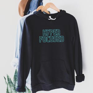May include: Black hooded sweatshirt with the text "HYPER FOCUSED" in teal blue outlined letters.