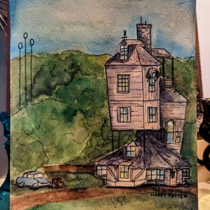 May include: A watercolor painting of The Burrow, the Weasley family home from the Harry Potter series. The house is a multi-level, crooked structure with a brown roof and a small car parked in front. The painting is signed "The Burrow Harry Potter".