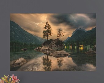 May include: A dramatic landscape photograph of a lake surrounded by mountains and trees. A lightning bolt strikes in the distance, illuminating the sky. Two small islands with trees are in the middle of the lake.