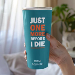 May include: A teal tumbler featuring the white and orange text "JUST ONE MORE BEFORE I DIE" stacked vertically, with an orange horizontal line underneath. The bottom of the tumbler displays the white text "MIAMI DOLPHINS" in a smaller font.