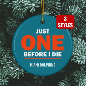 May include: A round teal ceramic ornament with a gold hanging string. The text reads JUST ONE BEFORE I DIE in bold orange and white letters, with MIAMI DOLPHINS printed below. A red rectangular badge in the corner displays the text 3 STYLES.