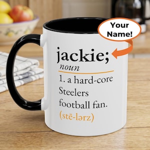 May include: A white ceramic mug with a black handle and interior rim. The front features black text reading: jackie; noun 1. a hard-core Steelers football fan. (stē-l&auml;rz). An orange arrow points to the text with an oval bubble saying Your Name!