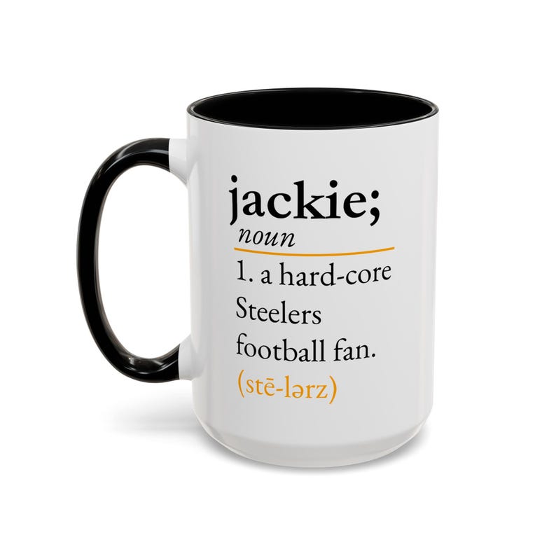 May include: A white ceramic mug with a black interior and handle. The front features black text that reads: jackie; noun 1. a hard-core Steelers football fan. (stē-l&auml;rz) with an orange horizontal line and phonetic pronunciation.