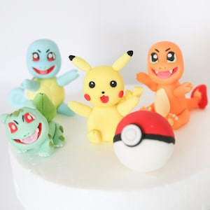 Puede incluir: Cinco personajes de Pokemon coloridos hechos de fondant, incluyendo Pikachu, Bulbasaur, Charmander, Squirtle y una Pok&eacute; Ball.