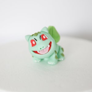 Puede incluir: Una figurita de fondant verde y roja de un personaje de dibujos animados con una amplia sonrisa y ojos grandes. La figurita es un personaje popular de una serie de anime y videojuegos japoneses.