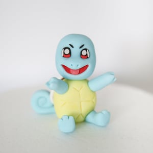 Puede incluir: Una figurita de Squirtle azul y amarilla con la lengua roja fuera. La figurita est&aacute; hecha de fondant y tiene un aspecto de dibujos animados.