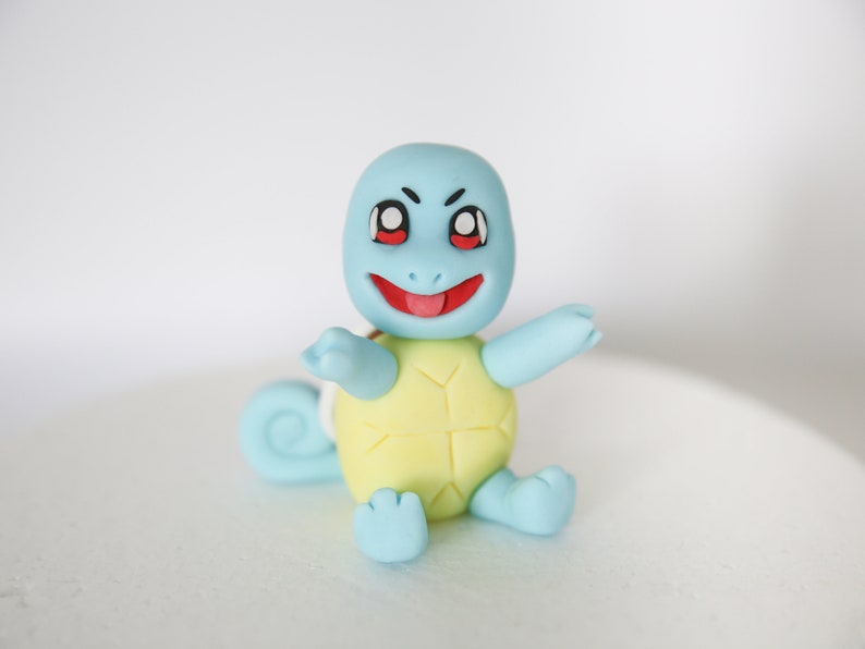 Puede incluir: Una figurita de Squirtle azul y amarilla con la lengua roja fuera. La figurita est&aacute; hecha de fondant y tiene un aspecto de dibujos animados.
