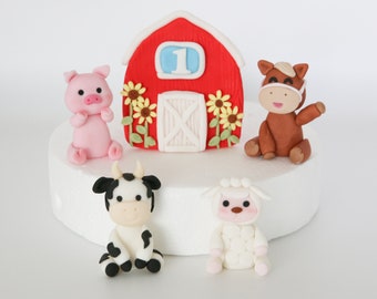 May include: A red barn cake topper with a white door and sunflowers. There are five fondant figurines: a pig, a cow, a sheep, a horse, and a number one.