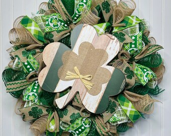 Op de afbeelding: Een groene, gouden en bruine St. Patricks Day krans met een houten klaverblad uitsnijding. De krans is gemaakt van jute, gaas en lint.