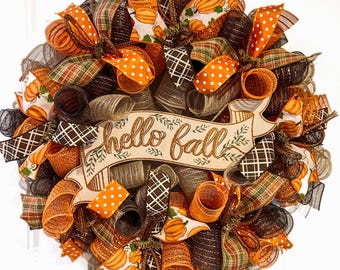 May include: A fall-themed wreath with a variety of ribbons in orange, brown, and green. The wreath features a banner that reads "hello fall" in gold lettering. Pumpkin and polka dot patterns are visible throughout the design.