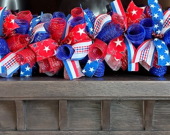 May include: A red, white, and blue patriotic door swag with mesh, ribbon, and star accents. The swag is decorated with red, white, and blue mesh, ribbon, and stars. It is perfect for adding a festive touch to your home for the Fourth of July or other patriotic holidays.