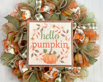 May include: A fall-themed wreath with orange, green, and brown burlap ribbon, mesh, and a sign that says "hello pumpkin".