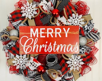 May include: A red, black, and white Christmas wreath with a sign that reads "Merry Christmas". The wreath is decorated with plaid ribbon, snowflake ornaments, and silver ornaments.